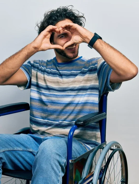 Disabled man in wheelchair making love heart shape with hands to camera