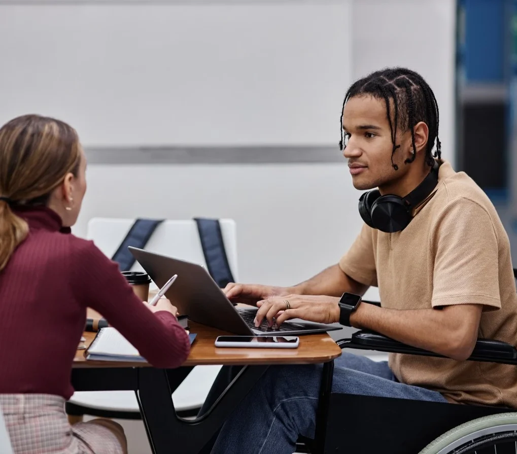 Disabled man in wheelchair using laptop and talking with support worker